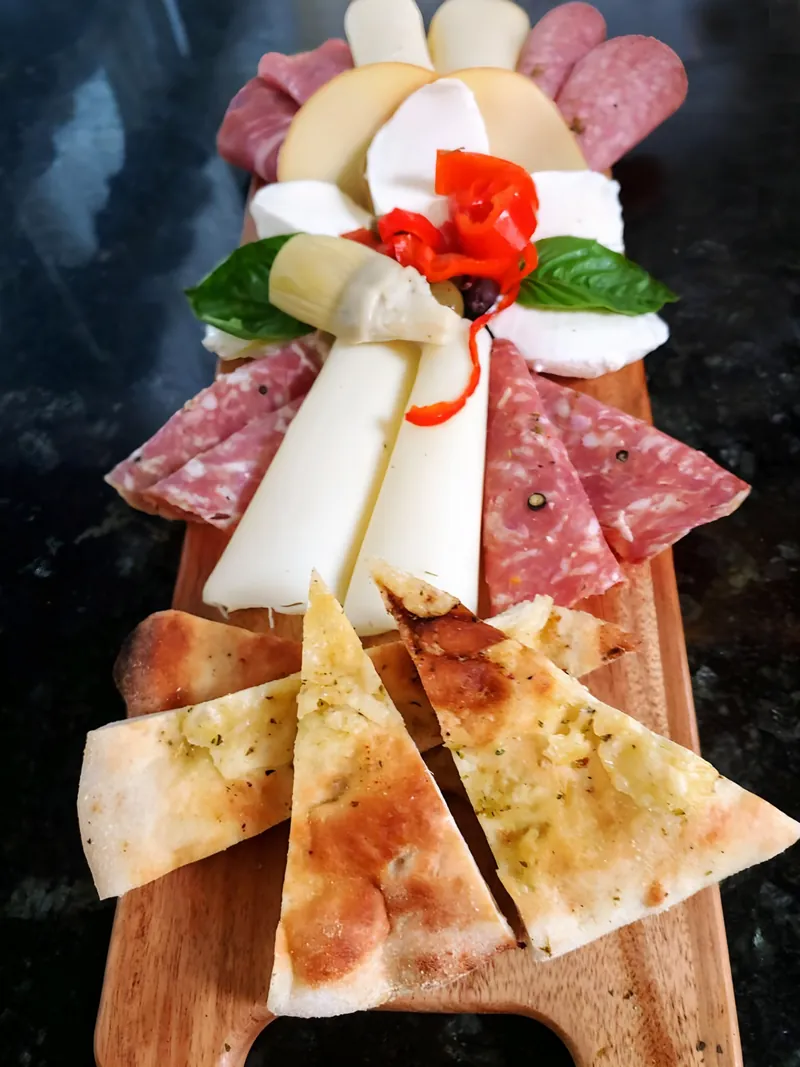 Antipasto board of salami, prosciutto and cheeses with crostini, a red pepper flower in the center