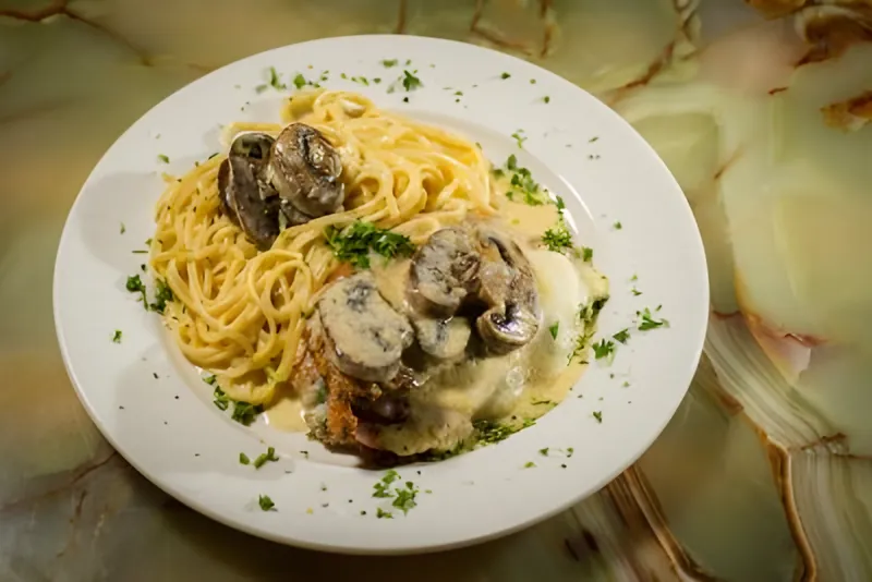 Breaded cutlet in a creamy mushroom sauce beside a nest of pasta