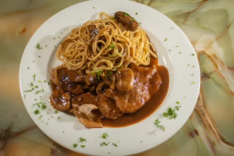 Spaghetti beside a cutlet in a browned mushroom sauce