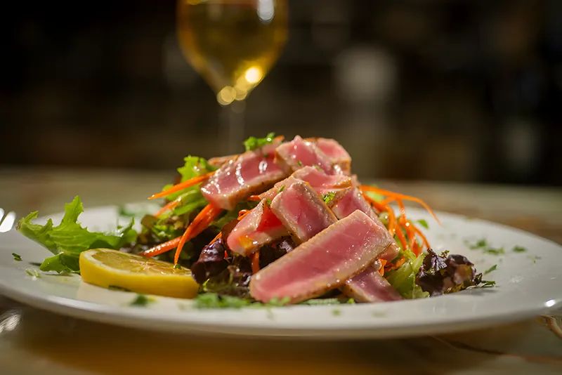 Seared tuna slices over mixed greens and shredded carrot with a lemon wedge